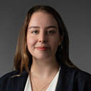 Pessoa adulta com cabelo liso e comprido usando blazer escuro listrado e blusa clara sorrindo levemente em fundo cinza. Yapay zeka taraf ndan olu turulan a  klama