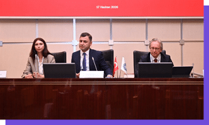 Tr s adultos sentados em uma mesa de confer ncia com microfones e laptops, com duas pequenas bandeiras no centro e um painel vermelho ao fundo indicando a data 17 de junho de 2026. Yapay zeka taraf ndan olu turulan a  klama