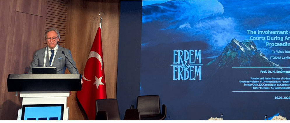 Pessoa adulta vestindo terno cinza est falando em um p lpito em um ambiente interno com uma bandeira da Turquia ao lado e uma tela grande ao fundo exibindo texto e imagens relacionadas a uma apresenta  o.  Yapay zeka taraf ndan olu turulan a  klama