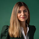 Pessoa adulta com cabelo liso e longo usando blazer escuro e camisa branca sorrindo em fundo verde. Yapay zeka taraf ndan olu turulan a  klama